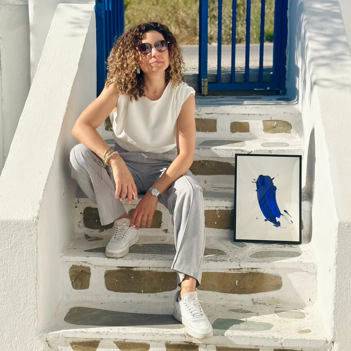 Florence Streif sitzen neben ihrem Kunstwerk in Blau auf Paros in Adelfia Studios. 